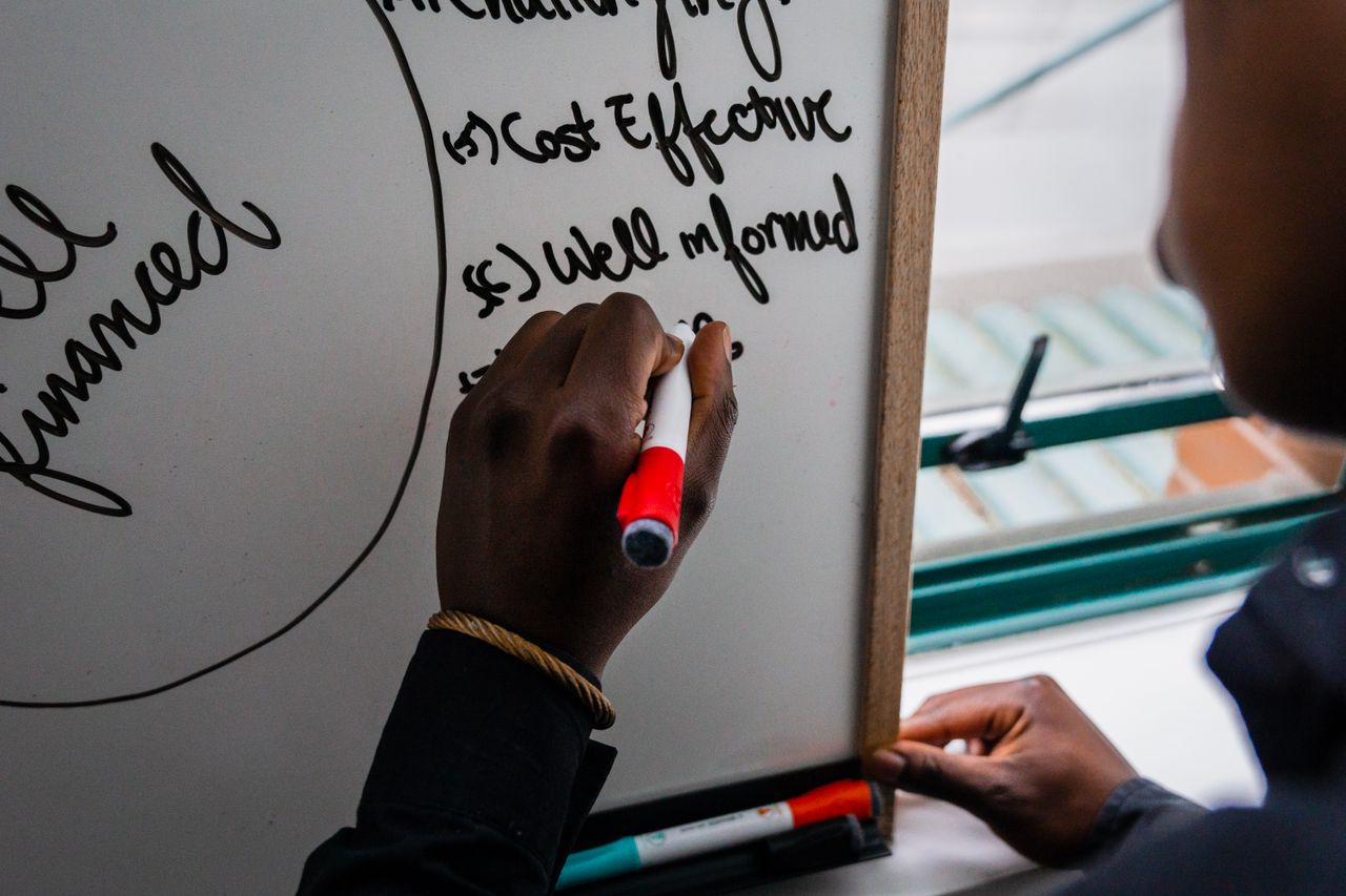 Hand writing on whiteboard with red marker, focusing on strategic planning keywords.